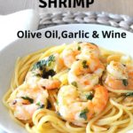 A white bowl filled with spaghetti with cooked shrimp, topped with parsley.