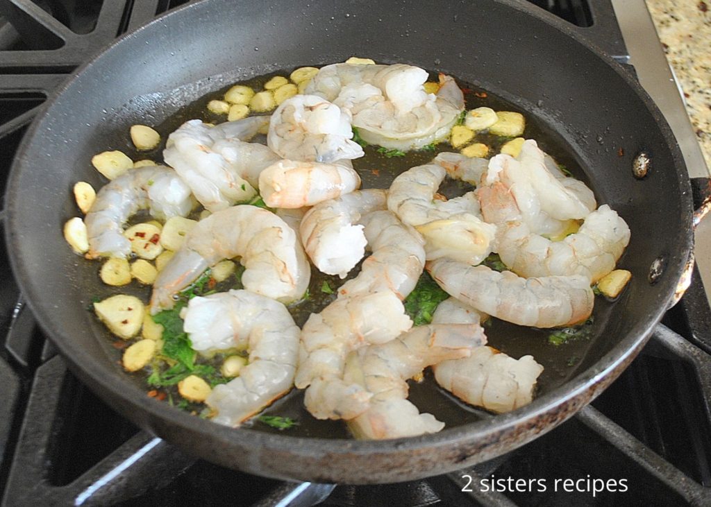 A skillet with raw shrimp and garlic.   by 2sistersrecipes.com