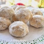 A white doily with a pile of round cookies covered in powdered sugar.