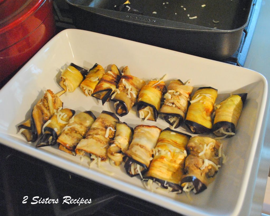 Eggplant slices are rolled and placed in a white baking dish. by 2sistersecipes.com 