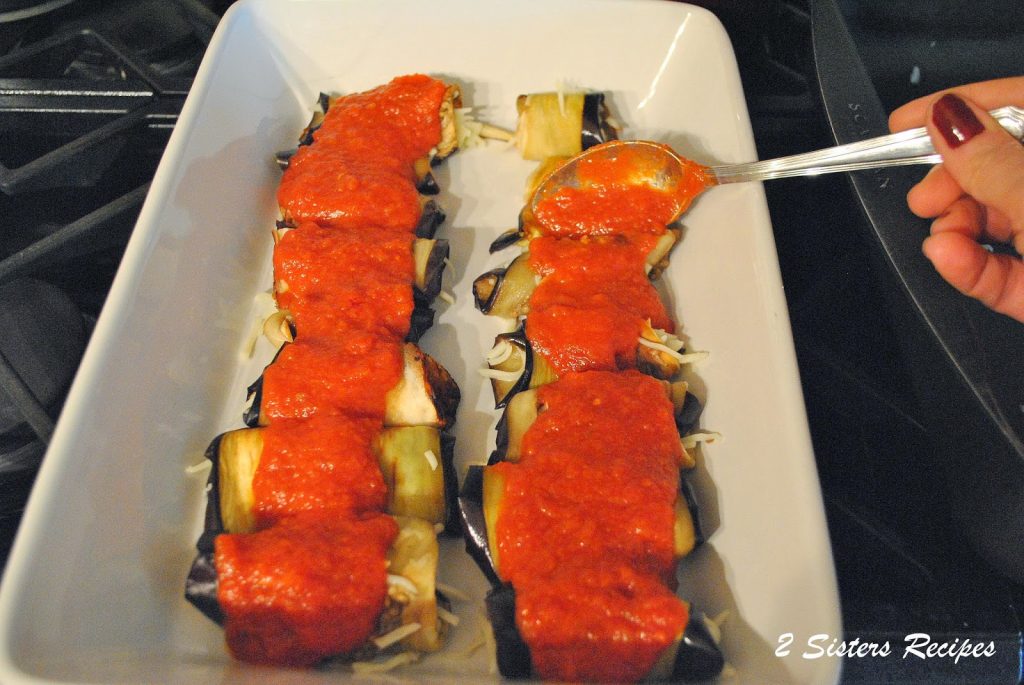 A white baking dish filled with eggplant rolled with cheese mixture and topped with tomato sauce.
