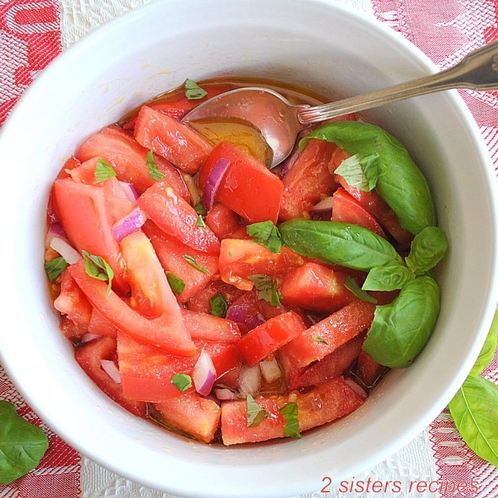 A white bowl filled with sliced fresh tomatoes and fresh basil.