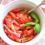 A white salad bowl filled with sliced fresh tomatoes, and fresh basil.