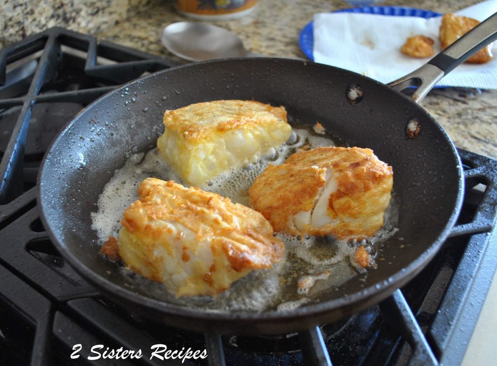 A black skillet frying up some cod in it.  by 2sistersrecipes.com 