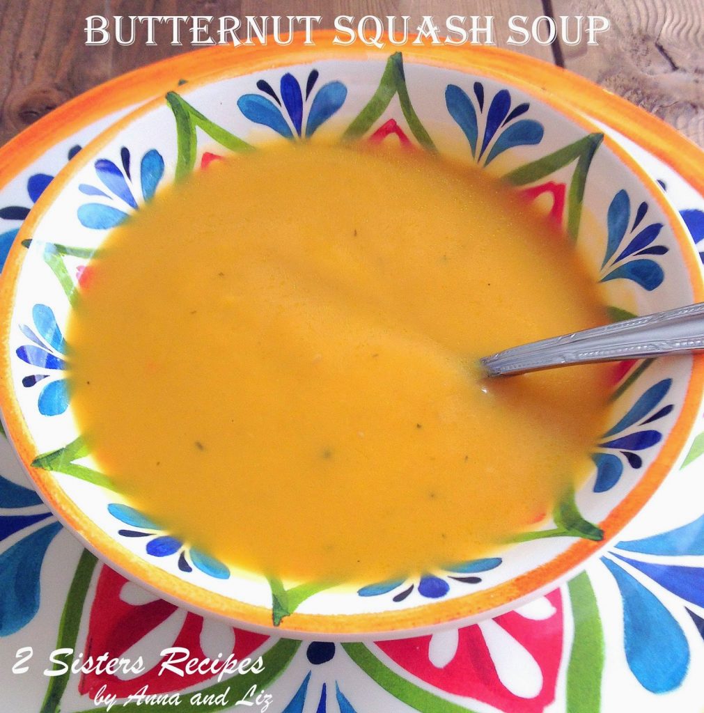 A colorful bowl of creamy butternut squash soup with a spoon inside the soup.