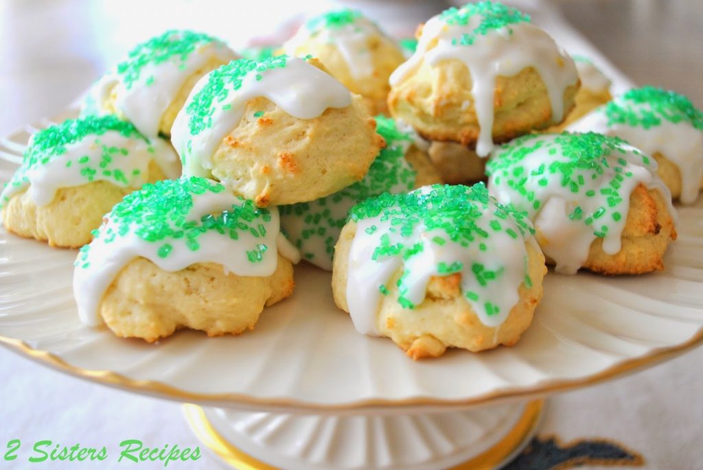 Italian Lemon Cookies with white glaze and green colored sprinkles on top, and displayed on a cake platter.