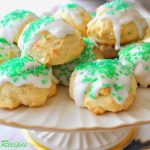 Italian Lemon Cookies with white glaze and green colored sprinkles on top, and displayed on a cake platter.