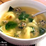 A white bowl filled with a soup, loaded with tortellini, mini meatballs and spinach.
