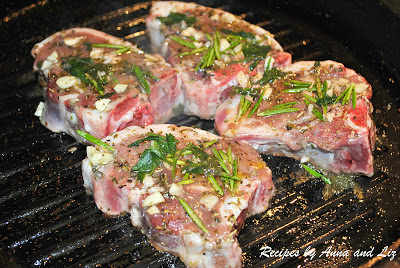 4 raw lamb chops cooking in a black iron skillet with herbs on top. 