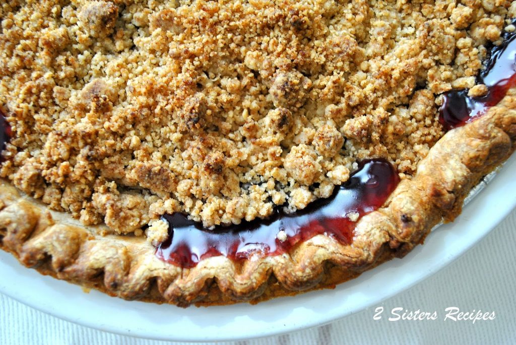A baked pie crust with blueberry juices oozing out, in a white pie dish. 