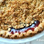 A baked pie crust with blueberry juices oozing out, in a white pie dish.