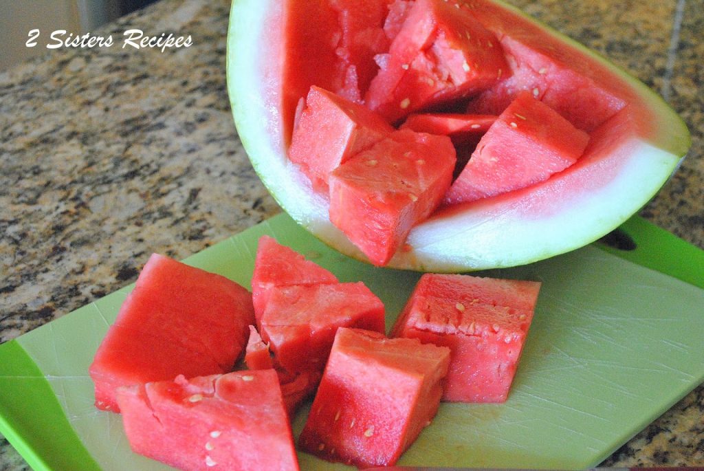 A watermelon cut into cubes on a green cutting board. by 2sistersrecipes.com 