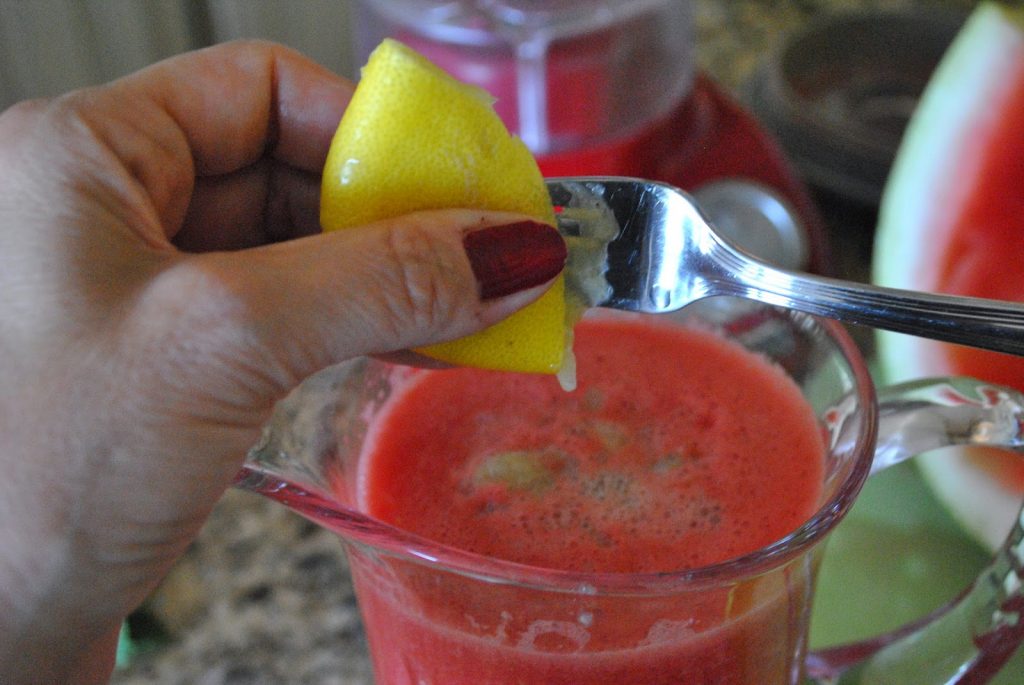 A fresh lemon is squeezed into a glass pitcher. by 2sistersrecipes.com 