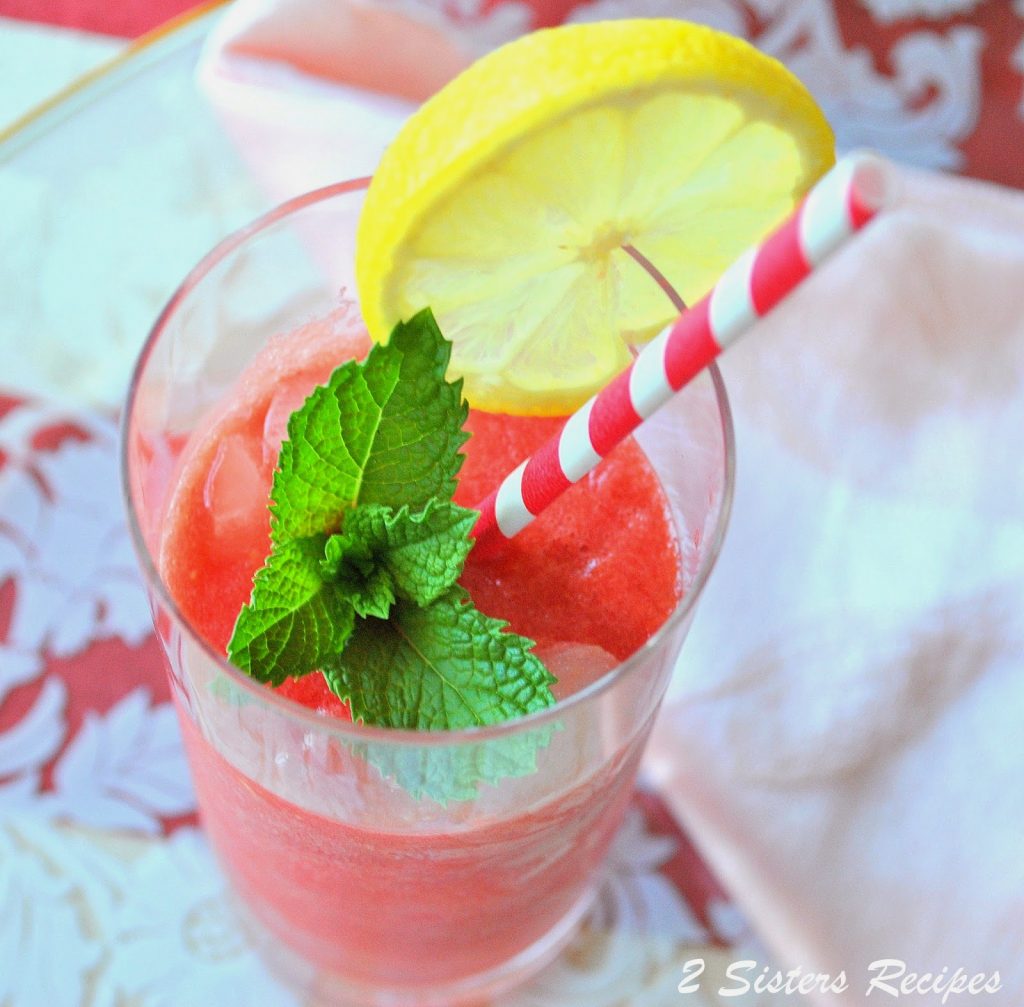 A tall glass filled with pureed watermelon and lemon juice and a slice of lemon and fresh mint on glass. by 2sistersrecipes.com