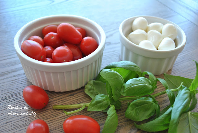 Two white bowls filled with cherry tomatoes, and small bocconcini balls and fresh basil on the table. 