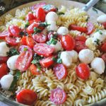 Fusilli pasta tossed with small mozzarella balls and cherry tomatoes in a large serving bowl.