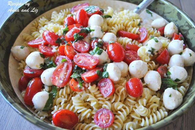 Fusilli pasta tossed with small mozzarella balls and cherry tomatoes in a large serving bowl.