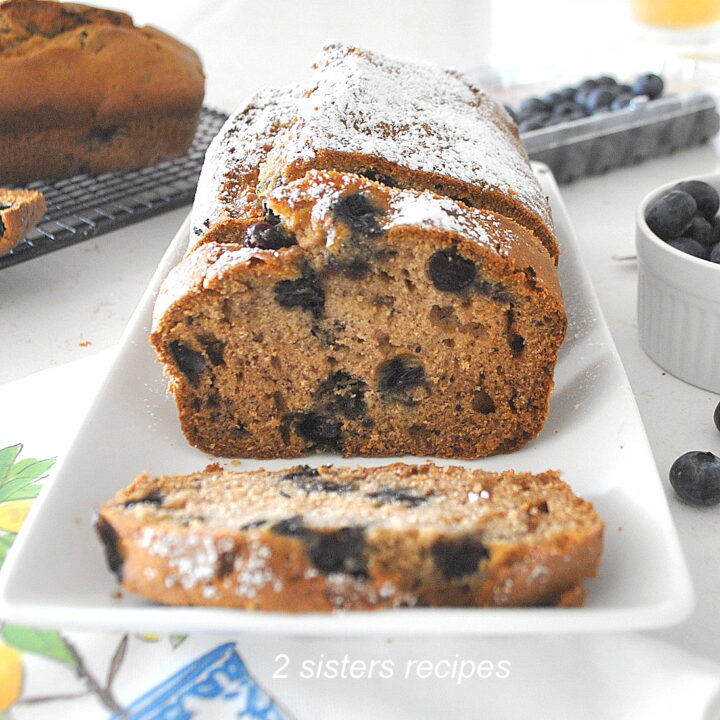 A blueberry banana bread is sliced on a long white platter.