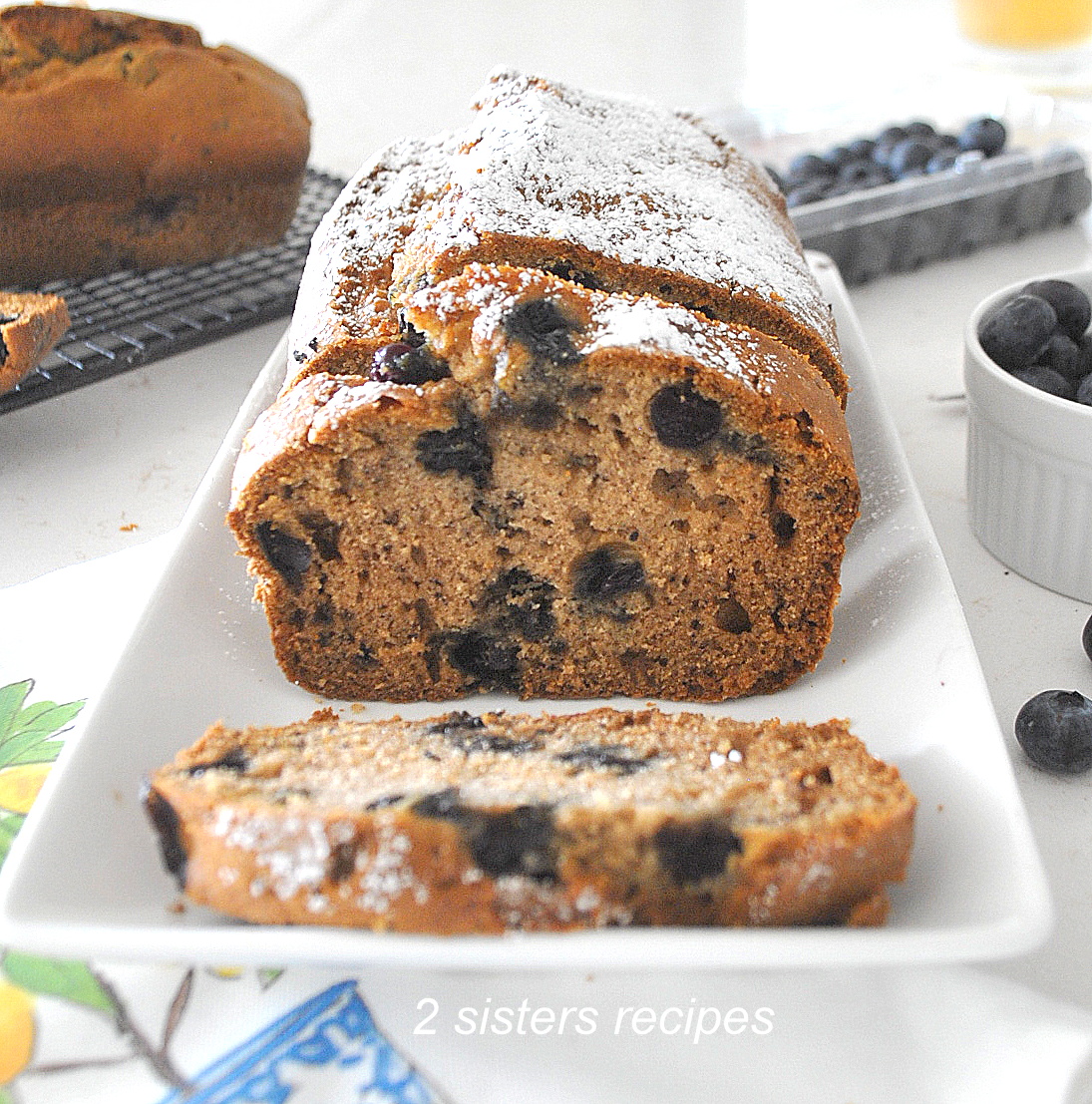 A blueberry banana bread is sliced on a long white platter.