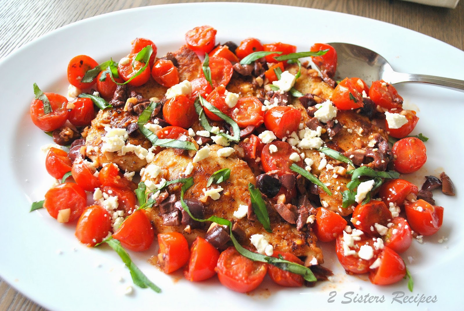 Chicken Cutlets with Cherry Tomatoes, Feta, Olives and Basil on a white serving platter.