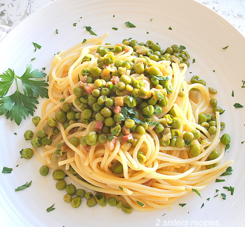 On a white plate is a serving of spaghetti tossed with baby peas and pancetta.