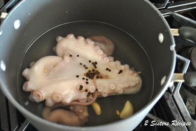 Raw octopus submerged in a pot filled with water and peppercorns. by 2sistersrecipes.com