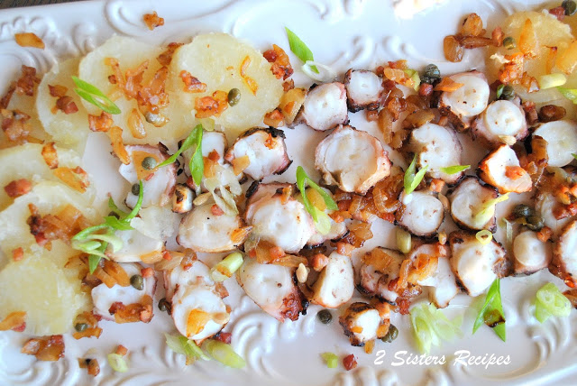 Sliced grilled octopus with sliced potatoes on a white platter. by 2sistersrecipes.com
