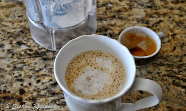 A coffee mug filled with frothy milk and espresso on the counter. by 2sistersrecipes.com