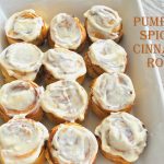 A white dish with 12 cinnamon rolls with icing on top.