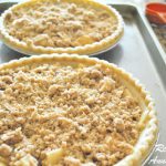 Two unbaked pie crusts filled with a filling, topped with a crumble, on a baking sheet.
