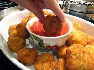 A rice ball is dipped into a small bowl of tomato sauce.