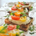 A white platter filled with crusty bread topped with burrata cheese, and cherry tomatoes.