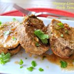 A pork tenderloin sliced on a white platter, served with a glazed, and lime wedges on the side.