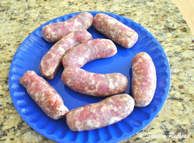 A blue plate with raw sausage links on it. by 2sistersrecipes.com