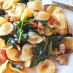 A plate filled cooked orecchiette pasta with sausages and spinach and cherry tomatoes.