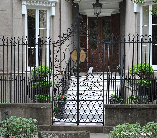 A black tall fence and gates, with a lovely design, guarding in front of a home.