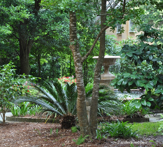 A Tall fountain with water streaming over, and palm trees in this small garden.