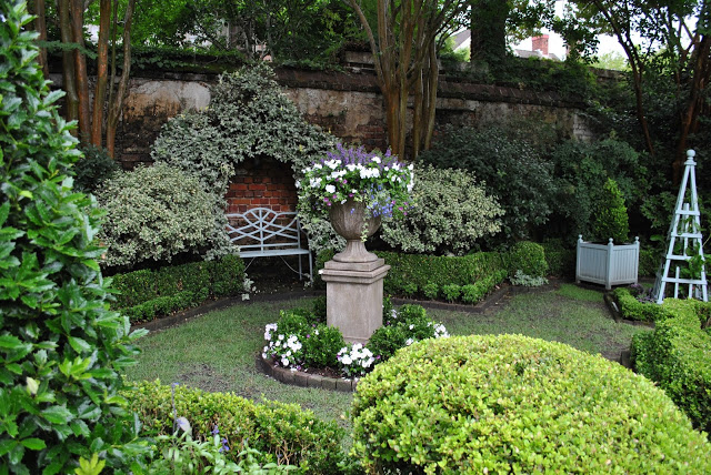A display of a garden with a tall Stone planter in the center of the garden.