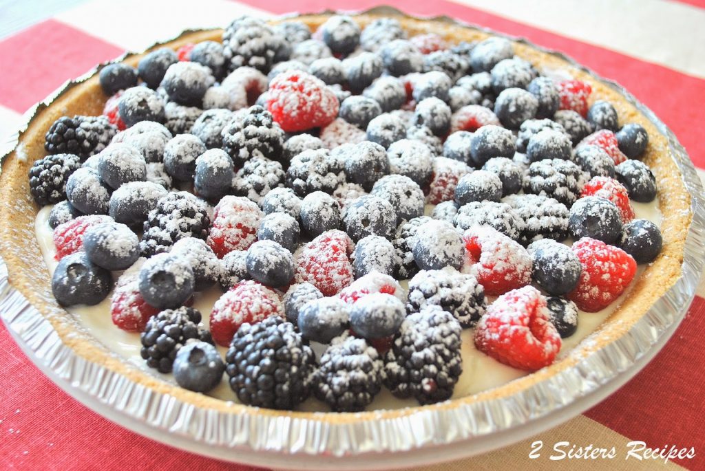 A pie topped with mixed berries and powdered sugar is served on the table.