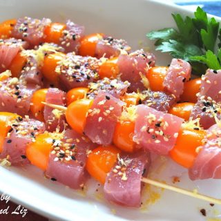 A white platter with four grilled tuna and cherry tomato kabobs.