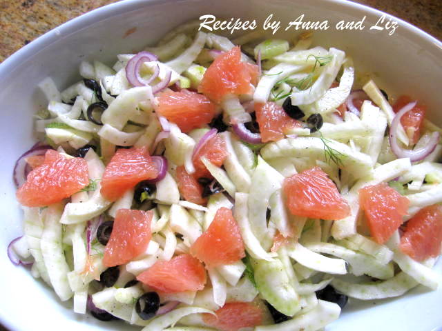 A large deep oval white bowl with sliced fennel and chunks of grapefruit and black olives.