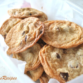 Baked, thin crispy chocolate chip cookies are placed in a plastic container.