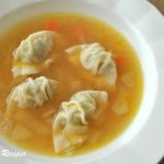A white bowl of chicken broth with min wontons floating in the soup.