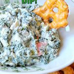 A white bowl filled with white and green creamy dip with thin pretzels around the bowl and one in the dip.