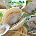 A dish filled with spaghetti topped with little neck clams and fresh parsley.