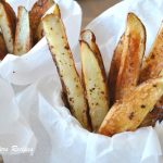 A cup with parchment paper and baked steak fries.
