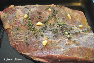 A raw brisket laid in a large roasting pan, topped with garlic, and fresh thyme sprigs.