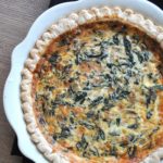 a white pie dish with a baked quiche filled with spinach and cheese.