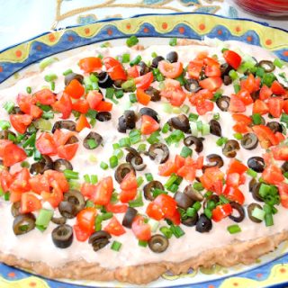 A colorful, oval shape platter filled with creamy mixture, topped with chopped green onions, cherry tomatoes, and black olives.