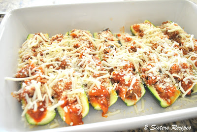 A white baking dish filled with raw zucchini boats with filling and cheese on top.